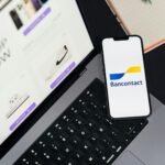 Smartphone displaying Bancontact app on laptop during online shopping.