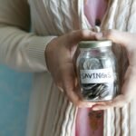 Woman holding a jar labeled 'savings' filled with coins, representing financial savings.